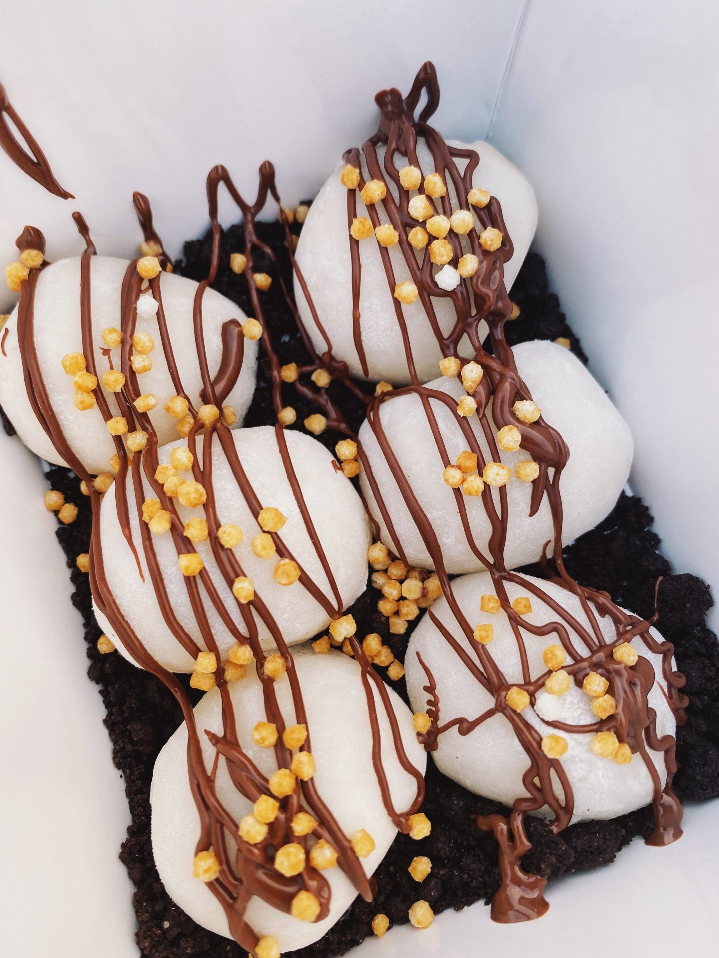 Vanilla mochi balls on a bed of Oreo cookie crumbs, drizzled with Nutella and popped rice sprinkles